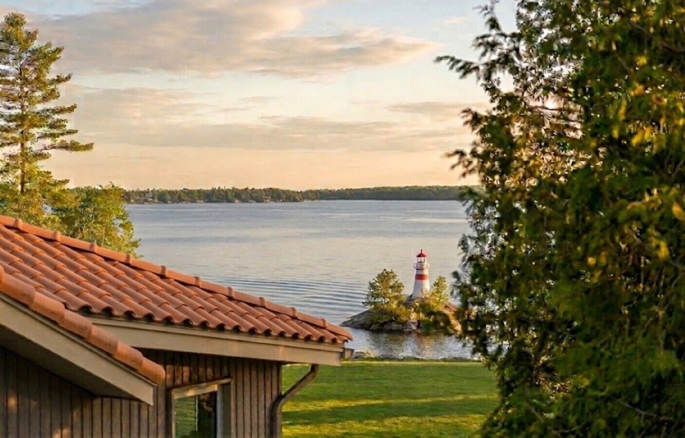 A lakeside view with a lighthouse, a wooden building with a tiled roof, and surrounding greenery.