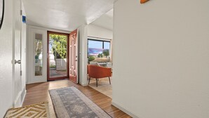 Un pasillo con piso de madera, un tapete y una puerta que da a un patio con una silla y vistas al exterior.