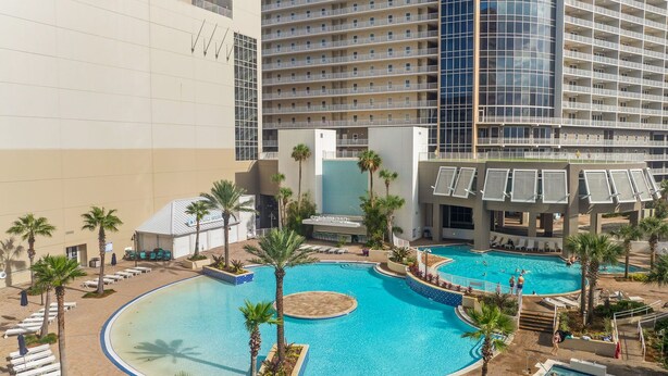 A hotel pool area with multiple pools, sun loungers, and palm trees.