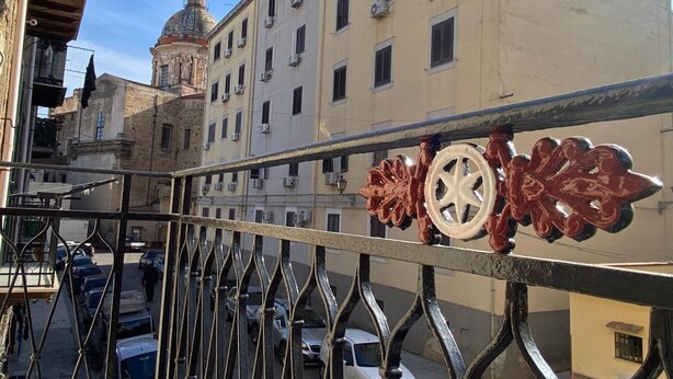 A street view with a building featuring a dome and a balcony railing with decorative elements. - GuestHost - Cozy 87 sqm apartment, for 6 people, located on the first floor of a building (NO lift). The accommodation is located in the heart of the historic Ballarò market (in a restricted traffic zone), an area where it is possible to savor the true  (Palermo)