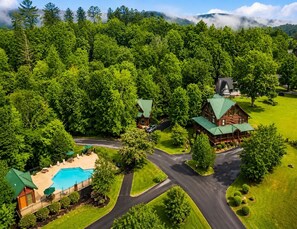 A lodge with a swimming pool, surrounded by lush greenery and a winding road.