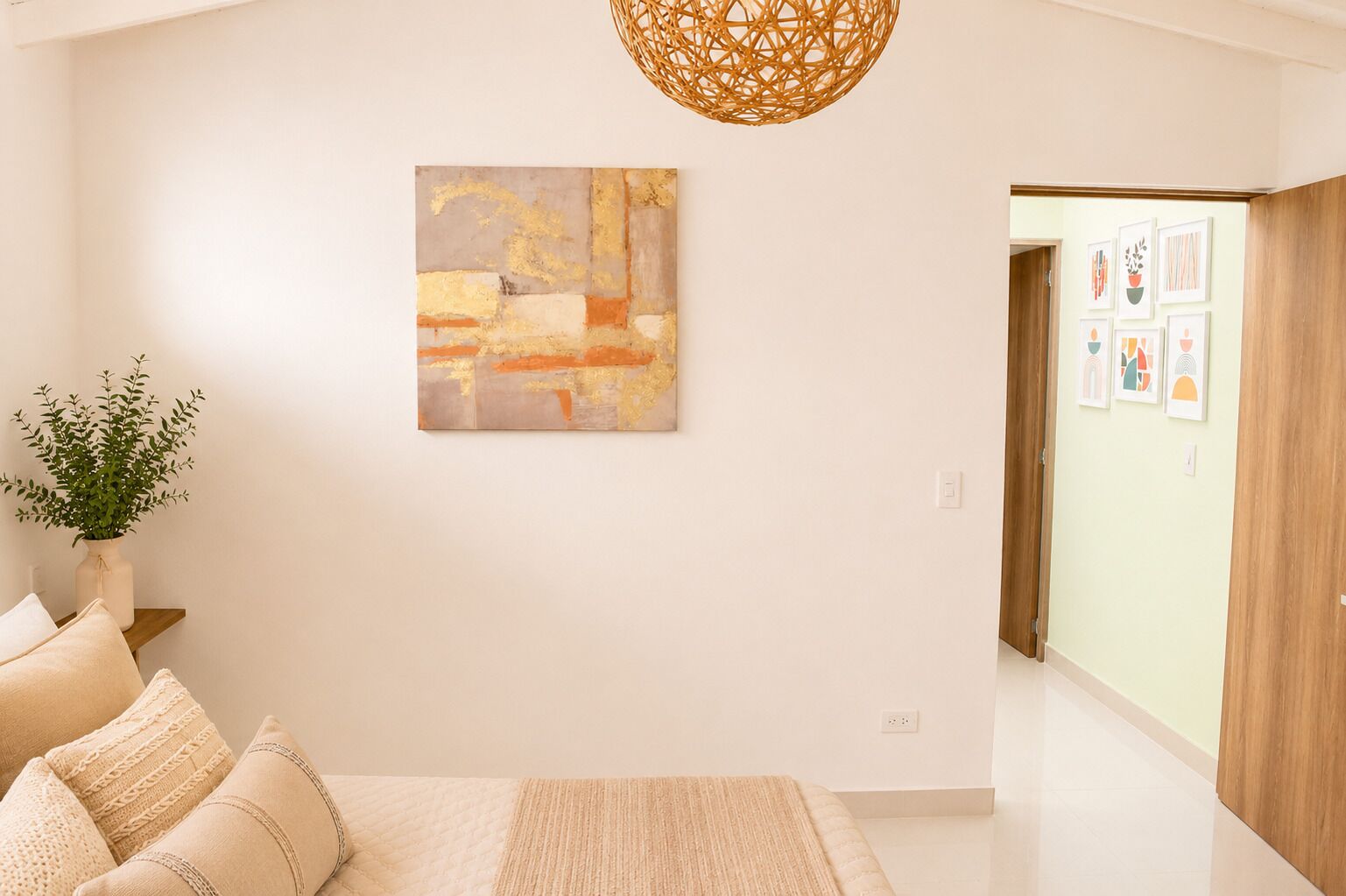 A modern bedroom with a bed, a wall-mounted abstract painting, a hanging woven light fixture, and a hallway leading to a door with framed artwork.