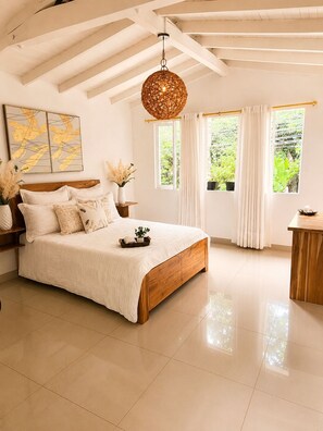 A bedroom with a wooden bed, a hanging light fixture, a window with curtains, and a wall with a framed artwork. - Classic Spacious Home, near Plaza Mayor and Laureles area.
Pet-Friendly. (Medellín)