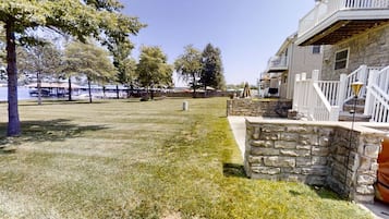 A backyard with a stone patio, a grassy lawn, and a building with a balcony.