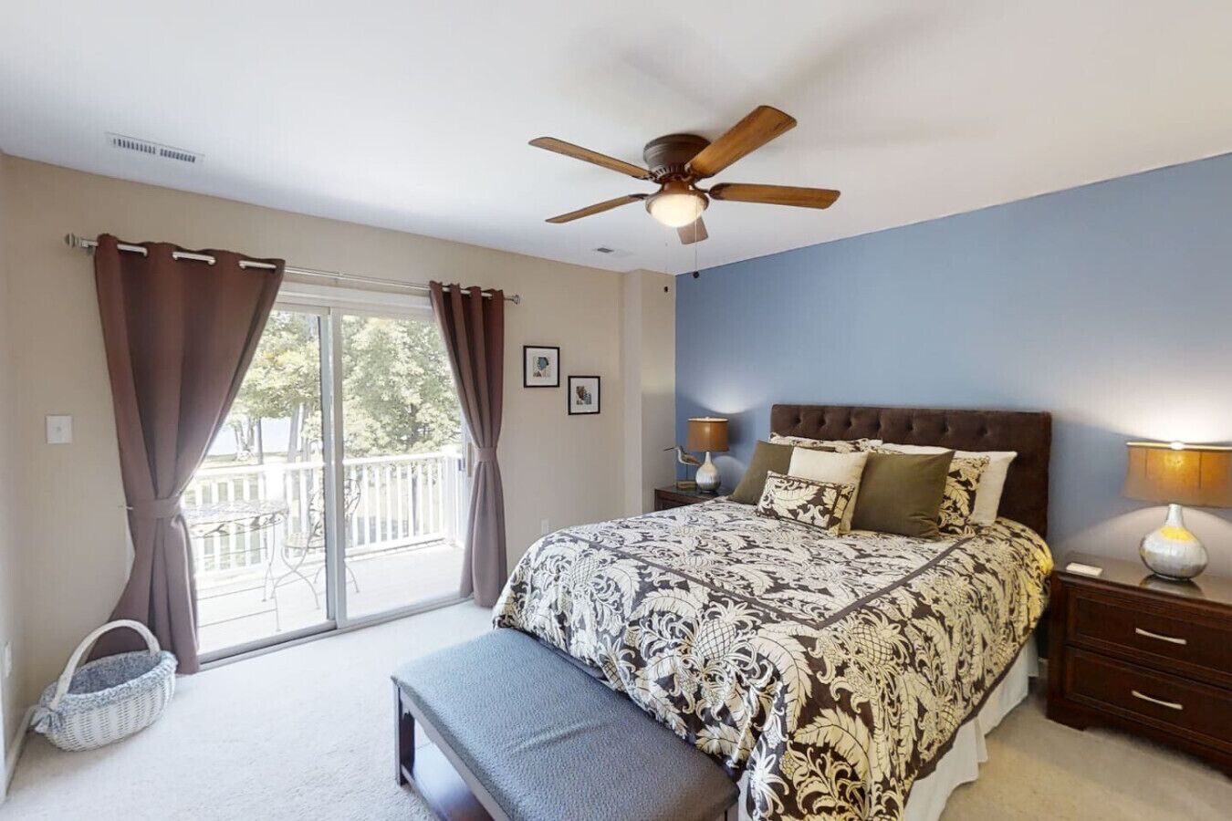 A bedroom with a large bed, a ceiling fan, a bench, and a view of a balcony.