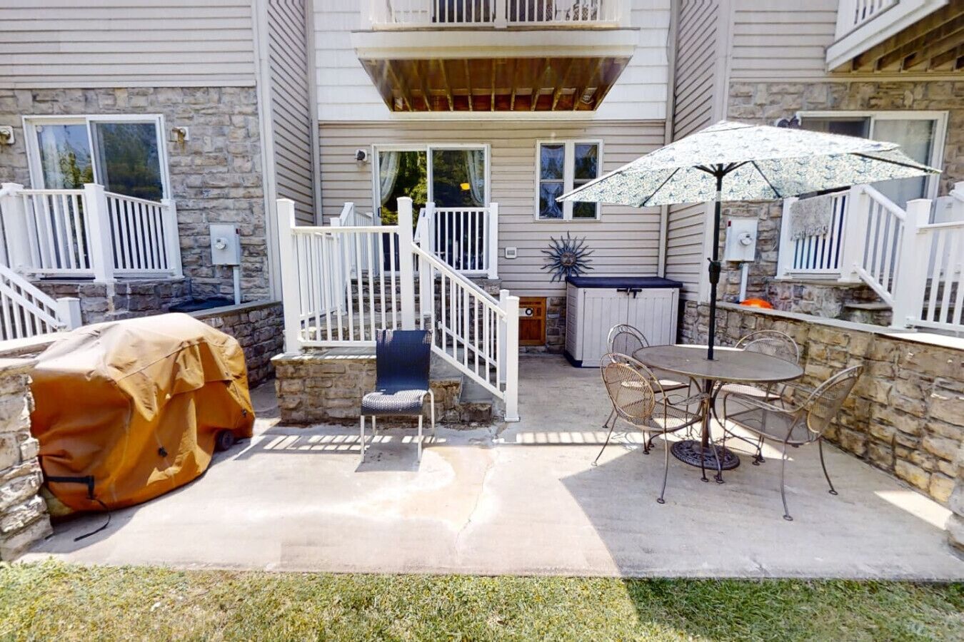 A covered patio with a table and chairs, a barbecue grill, and a decorative umbrella.