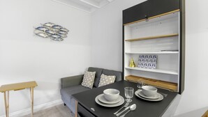 A modern room with a grey sofa, a dining table set with plates, glasses, and cutlery, and a wall-mounted shelf with decorative items. - 1 Bedroom bolthole in Seahouses (Seahouses)