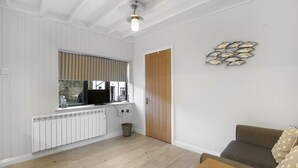A room with a wooden floor, a white radiator, a television on a window sill, a wooden door, and a wall-mounted decorative fish sculpture. - 1 Bedroom bolthole in Seahouses (Seahouses)