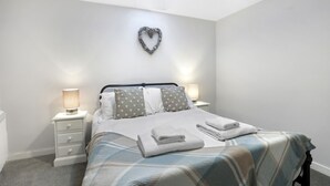 A neatly arranged bedroom with a bed, two bedside tables, a wall-mounted heart decoration, and a ceiling light. - 1 Bedroom bolthole in Seahouses (Seahouses)