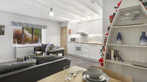 A modern kitchen with white cabinets, a dining area with a table set for two, and a cozy living room with a sofa. - 1 Bedroom bolthole in Seahouses (Seahouses)
