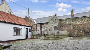 A stone building with a red-tiled roof, a white building with a red door, and a cobblestone courtyard. - 1 Bedroom bolthole in Seahouses (Seahouses)