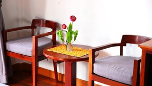 Une table de salle à manger en bois, accompagnée de deux chaises, d’un vase avec des fleurs et d’un set de table jaune.