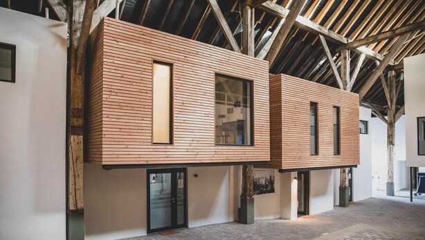 A modern building with wooden paneling, large windows, and a high ceiling with exposed beams.