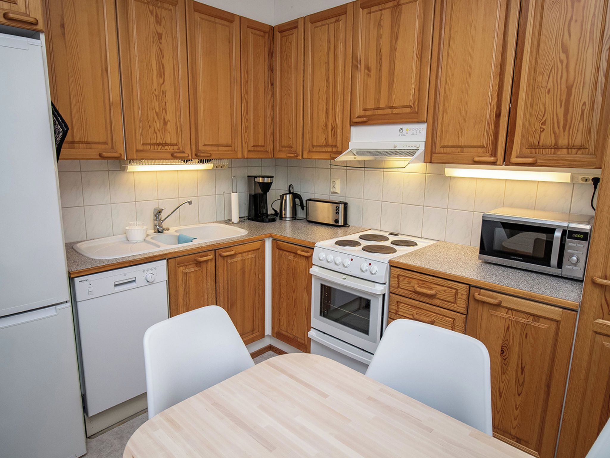 A compact kitchen with wooden cabinets, a white stove, a microwave, and a sink.