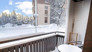 Un balcon donnant sur une rue et des arbres couverts de neige, avec une chaise et une petite table.