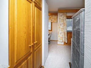 Ein schmaler Flur mit Holztüren und Fliesenboden, der zu einem Raum mit Fenster und Stuhl führt.