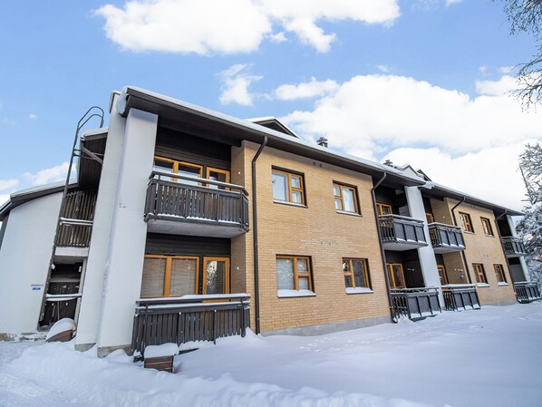 A multi-story building with balconies, a brick facade, and snow on the ground.