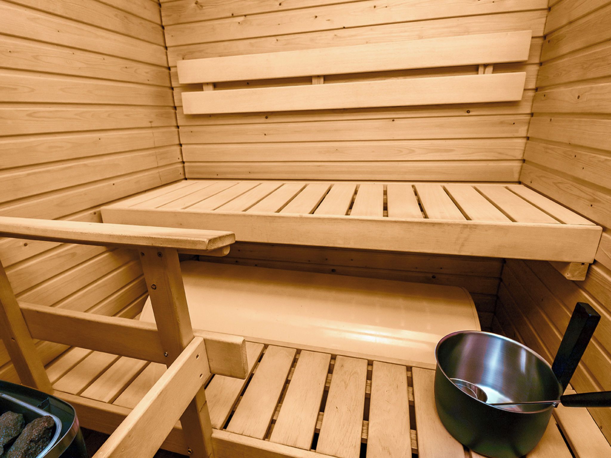 Una sauna con bancos de madera y un recipiente metálico.