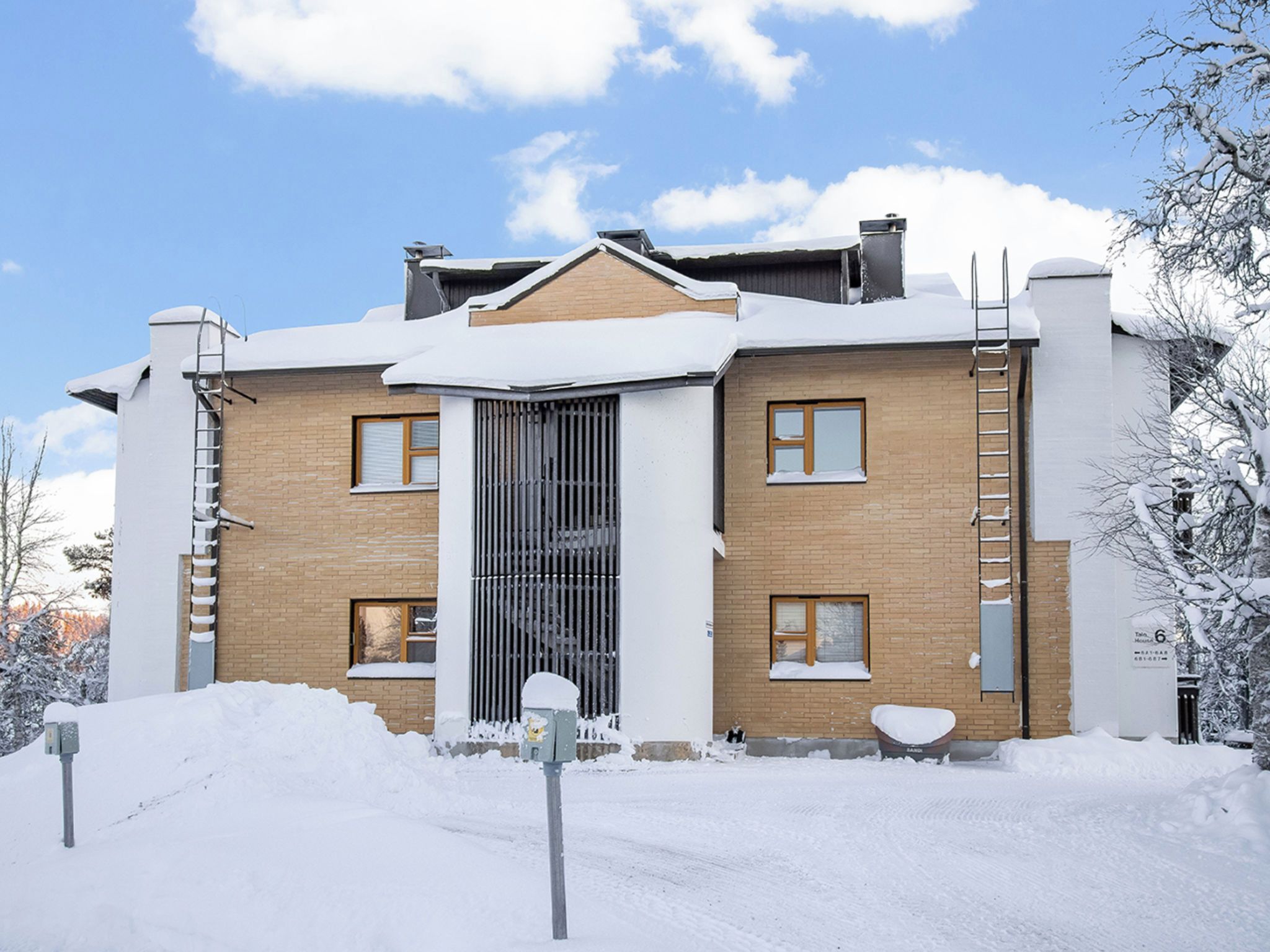 A two-story building with a brick facade, a central entrance with a metal gate, and a snow-covered roof.