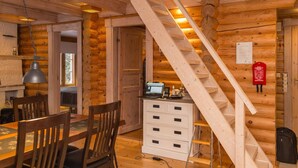 Een houten chaletinterieur met een eethoek, een bureau met een computer, een trap en een brandblusser.