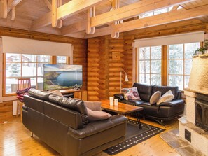A log cabin interior with a leather sofa, a television, and a fireplace.