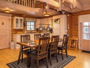 A wooden interior with a dining table, chairs, and a kitchen area.