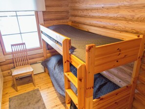 A small wooden cabin room with a bunk bed, a chair, and a window.