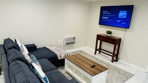 Un salon moderne avec un canapé gris, une table basse en bois et un téléviseur à écran plat fixé au mur.