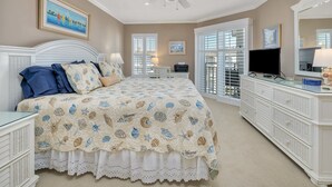 A bedroom with a bed, a ceiling fan, a dresser, a television, and a window with shutters. - Enjoy Island Living at Oceanfront Condominium! Inc (Saint Simons Island)