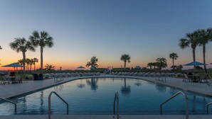 A swimming pool with lounge chairs and palm trees, surrounded by umbrellas. - Enjoy Island Living at Oceanfront Condominium! Inc (Saint Simons Island)