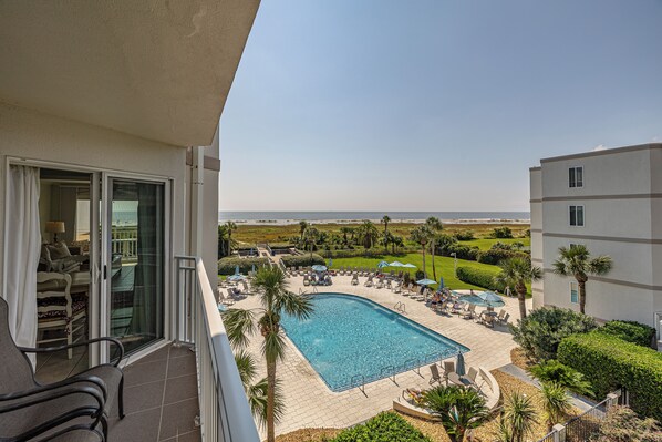 A pool area with lounge chairs and umbrellas, surrounded by greenery and a view of the ocean.