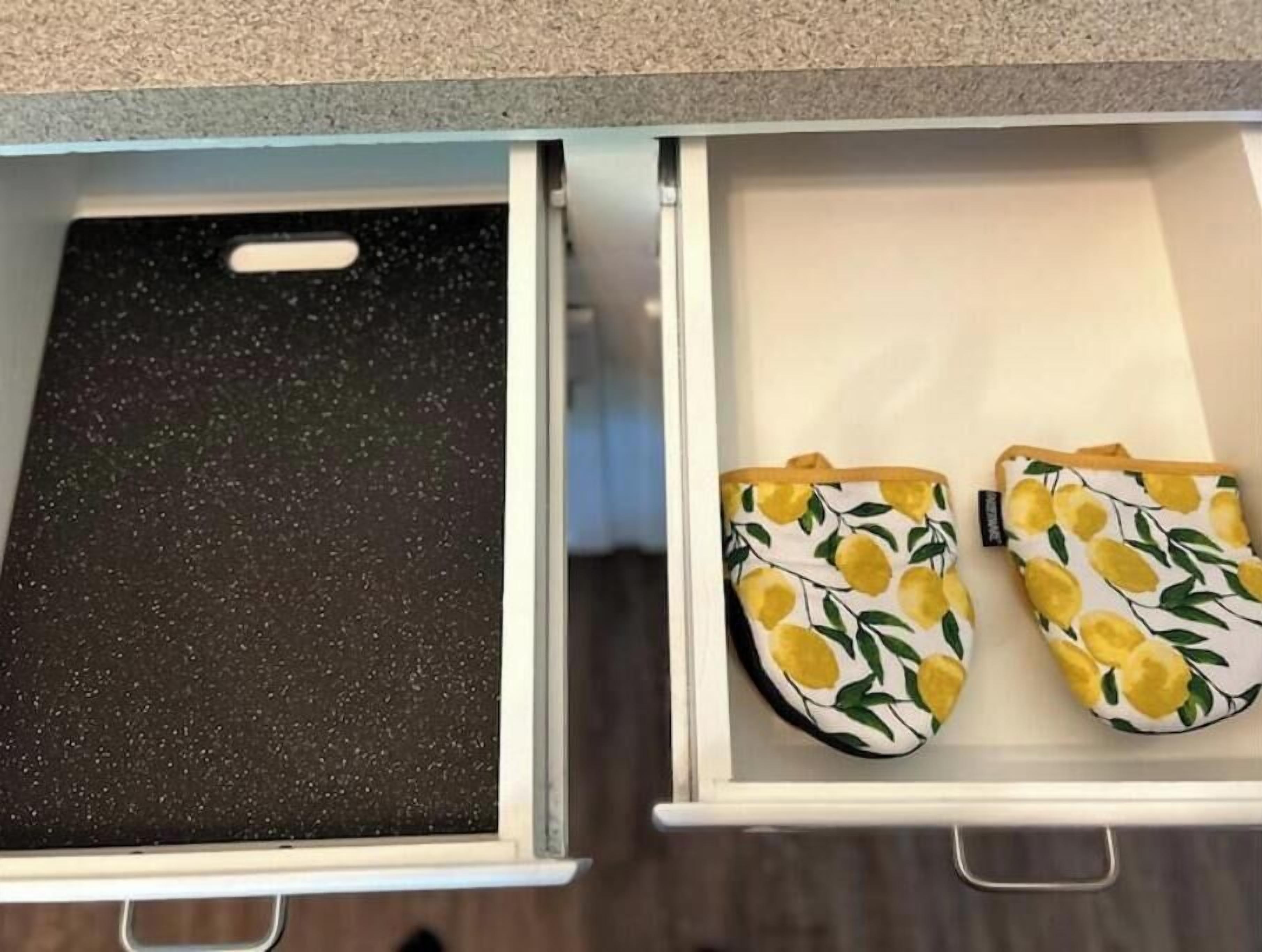 Un tiroir de cuisine avec un pare-éclaboussures à motifs et une paire de maniques de cuisine jaunes et vertes.
