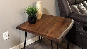 Una pequeña mesa de madera con una planta en maceta y un florero, ubicada junto a un sofá de cuero en una habitación con un espejo grande y un cuadro en la pared.