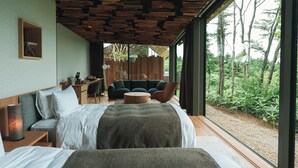 Une chambre moderne avec un grand lit, un bureau et un canapé. La fenêtre offre une vue sur la verdure.