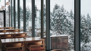 Un restaurant avec des tables et des chaises en bois, de grandes fenêtres et une vue sur des arbres couverts de neige.