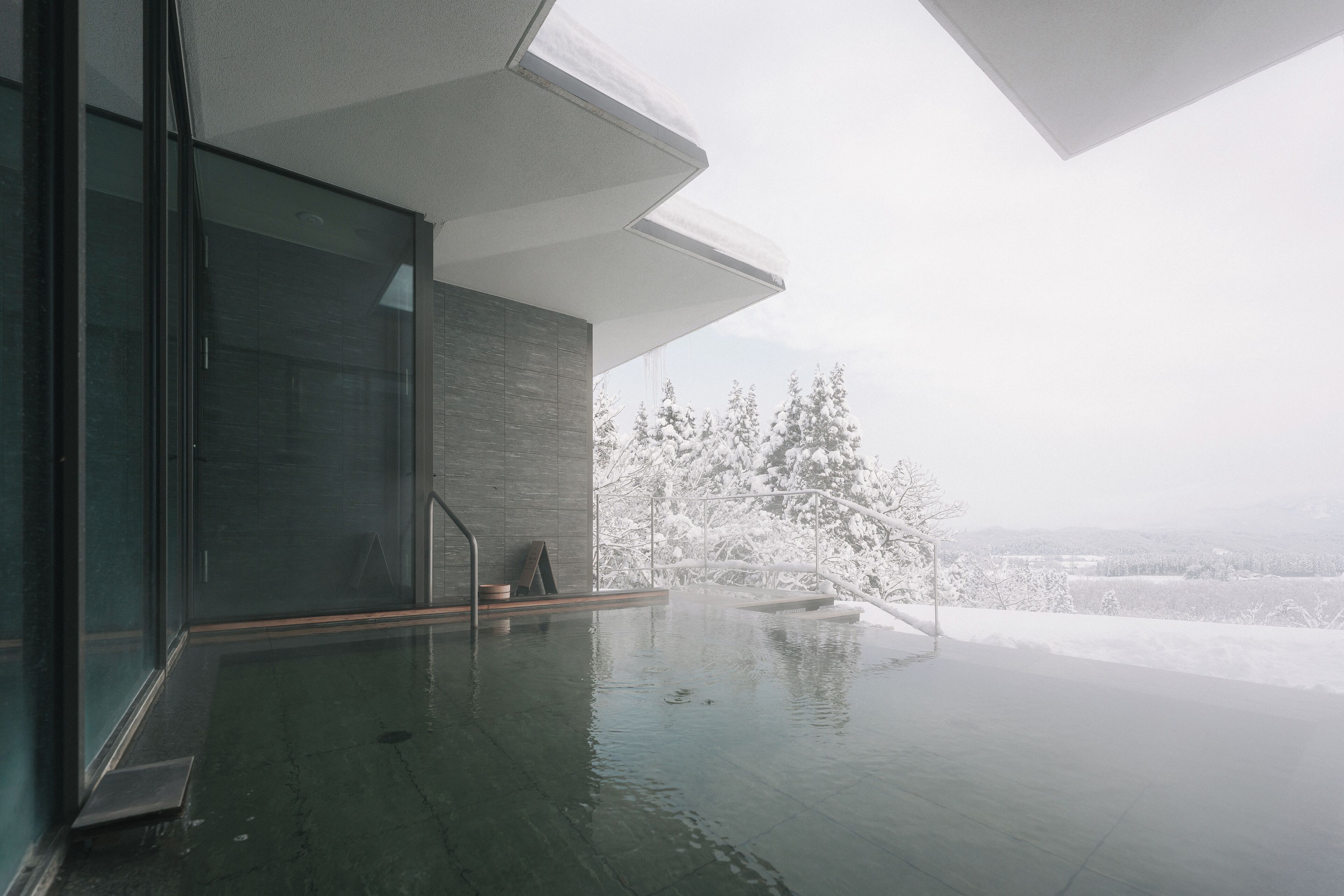 A modern indoor pool with glass walls and a view of snow-covered trees.