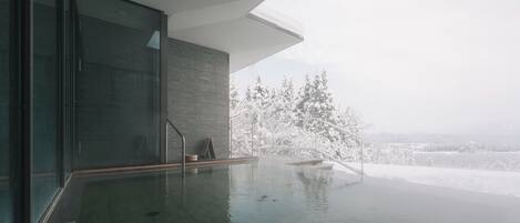 A modern indoor pool with glass walls and a view of snow-covered trees.