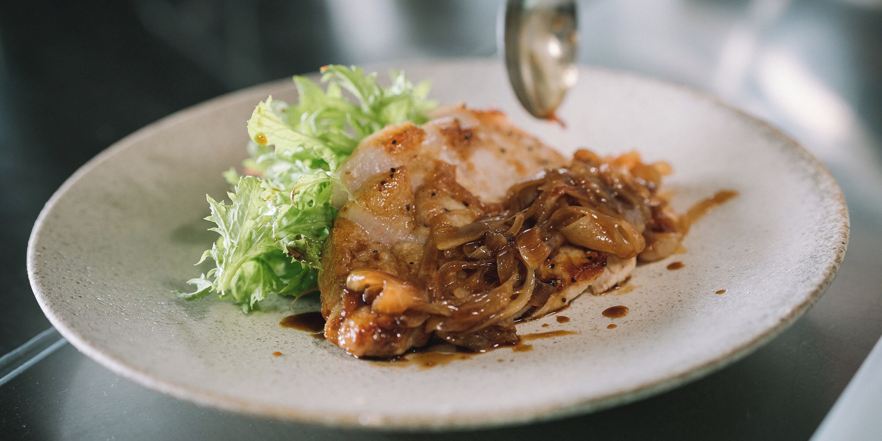 A plate with a grilled chicken breast, onions, and a side of lettuce.