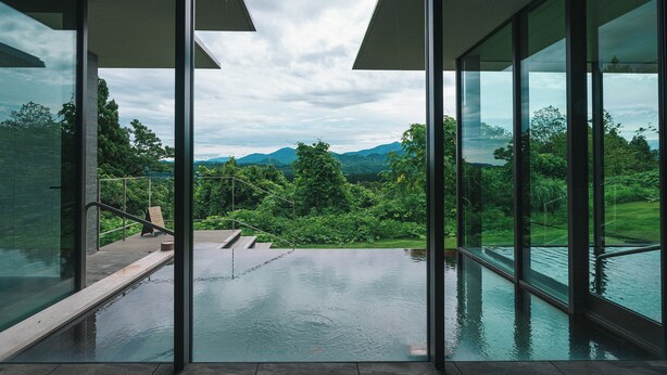 Une piscine à débordement moderne offrant une vue sur une végétation luxuriante et des montagnes.