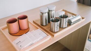 Un plateau en bois avec des thermos en acier inoxydable, une tasse rose et un carnet blanc avec un stylo.