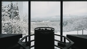 Une pièce dotée de grandes fenêtres donnant sur un paysage enneigé, un banc en bois et un objet cylindrique placé au centre.