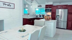 A modern kitchen with red cabinets, a white island, and a chandelier. - Home away from Home- The Willow Serenity Home (San Antonio)