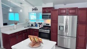 A modern kitchen with red cabinets, stainless steel appliances, and pendant lighting. - Home away from Home- The Willow Serenity Home (San Antonio)