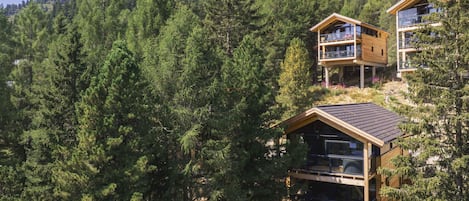 Una cabaña de madera moderna con balcón, rodeada de un bosque denso.