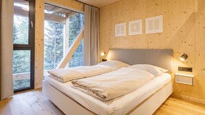 Un dormitorio con dos camas, paredes de madera, un ventanal y vistas a árboles.