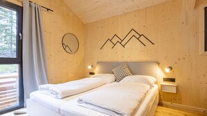 Un lit double avec du linge de lit blanc, dans une pièce aux murs en bois et ornée d’un motif représentant une montagne.