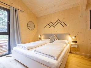 A double bed with white linens in a room with wooden walls and a mountain design on the wall.