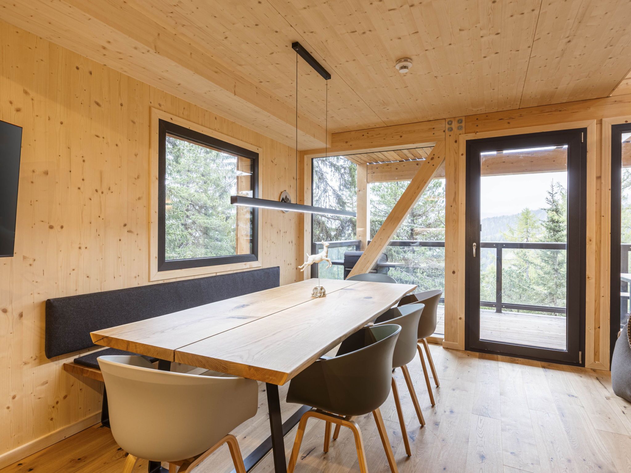 Un intérieur en bois comprenant une table à manger, des chaises et de grandes fenêtres donnant sur la forêt.