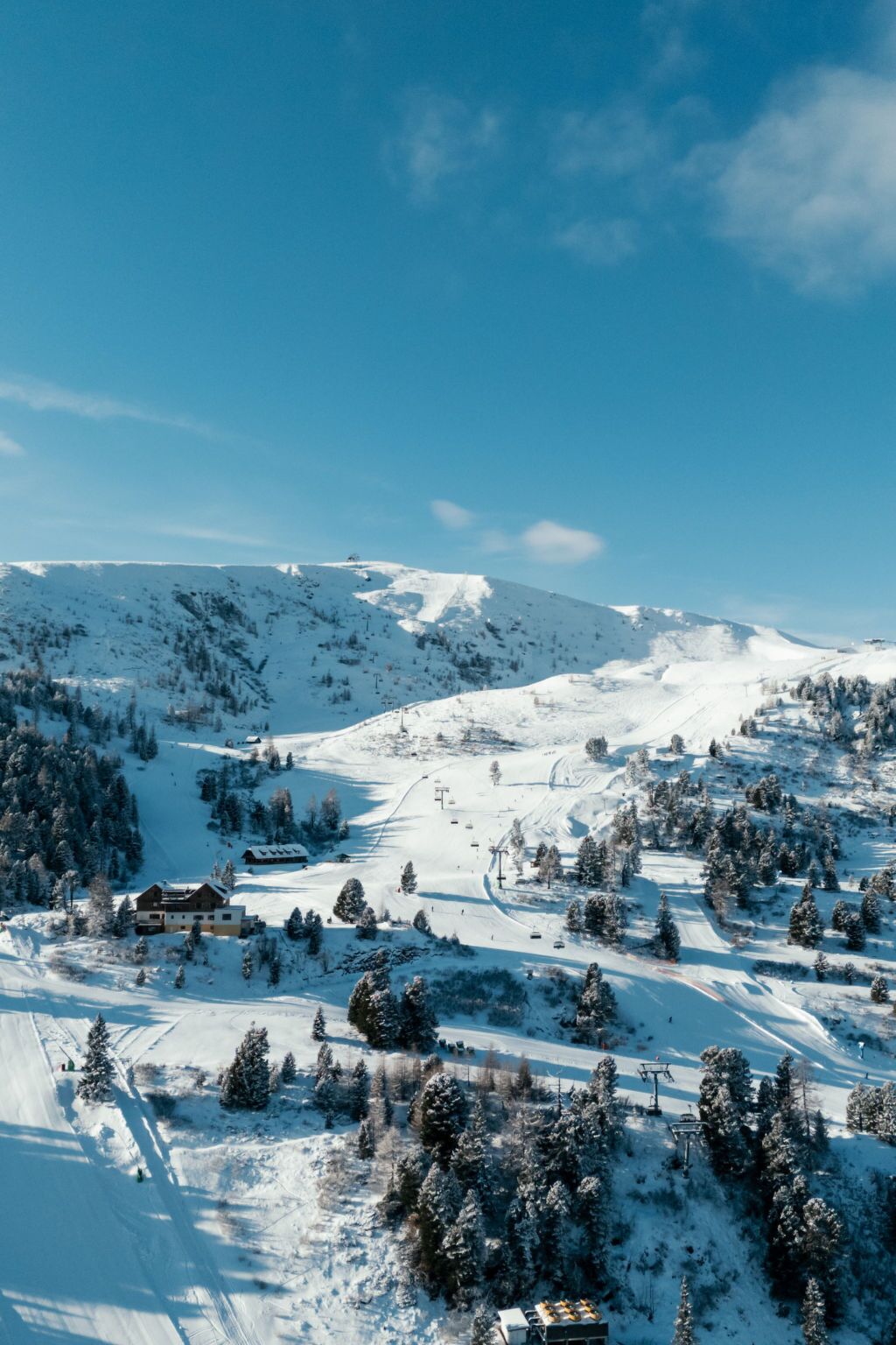 A snow-covered mountain landscape with ski slopes, a lodge, and a clear blue sky.