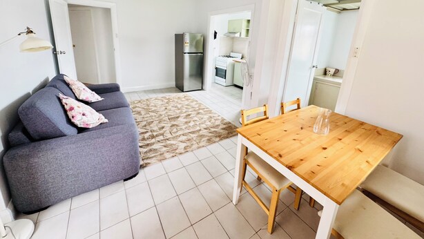 Un espace de vie compact avec un canapé gris, une table à manger en bois et un coin cuisine à l’arrière-plan.